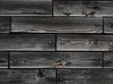 Eski gri yüzlü tahtaların dokusu. Yatay tahtalardan yapılmış bir köy evinin siyah ahşap duvarının parlak bir arka planı güneşte solmuş..