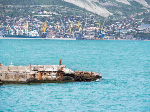 An old concrete pier destroyed by sea water against the background of the Black Sea. An abandoned pier littered with rocks.