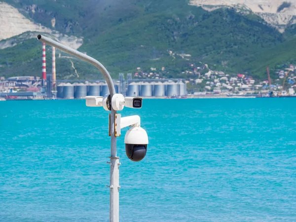 Many street surveillance cameras hang on a pole against the background of the sea. A video monitoring camera on the city embankment. CCTV in the port, factory. The concept of security resort