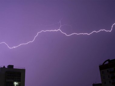 Yüksek binaların arka planına karşı tek atışta birkaç yıldırım düştü. Gece fırtınalı ve fırtınalı bir gece. Uzun pozlu kompozit fotoğraf.