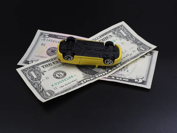 Road accident, car insurance, car expenses. The repair of the vehicle. Yellow broken toy car upside down on dollar bills.