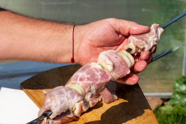 Bir adam elinde soğanla çiğ et turşusu tutar ve metal bir şişin üzerine koyar..