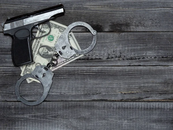 Firearm gun with dollar bills and police handcuffs are lying on the wooden background of the table. Concept of police corruption, black market, money crime.