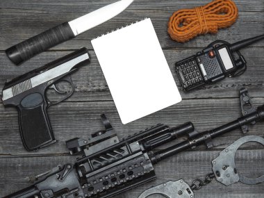 Bir muharebe otomatik tüfeği, bir polis tabancası ve beyaz not defterli bir masanın ahşap zemininde taşınabilir bir radyo. Hava yumuşaklığı ekipmanlarının düz yerleşimi.