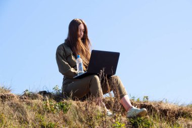 Dizüstü bilgisayarı olan bir kız şehrin dışındaki bir parkta çimlerin üzerinde oturuyor. Serbest çalışma, uzaktan çalışma ya da eğitim kavramı. Bağımsız bir kadın işadamı doğada seyahat ediyor..