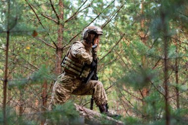 Askeri teçhizatlı bir kız, askeri eğitim alanındaki bir orman kampında engelli parkurdan geçiyor..