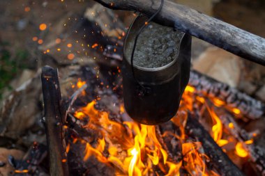 Karanlıkta askeri bir çömlek yanıyor. Çaydanlıkta yemek pişirmek ya da ormanın arka planında kamp ateşi yakmak. Hayatta kalma ve turizm.