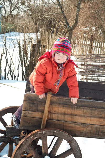 Little girl child in a wooden cart on a winter background — ストック写真