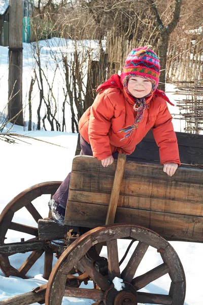 Little girl child in a wooden cart on a winter background — ストック写真