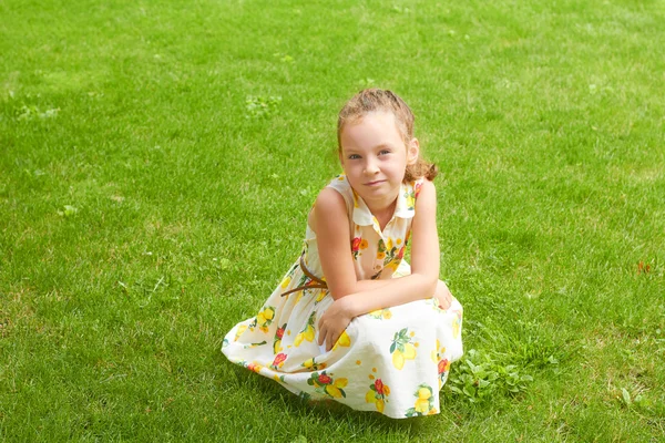 Pequena menina bonita em vestido na grama verde no parque — Fotografia de Stock