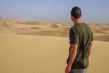 Sırtüstü çöl ortasında kumullara bakan bir turist.