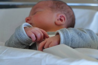 Bebek hastanedeki beşiğinde, bebeğin ellerinin detaylarına dikkat ediyor.