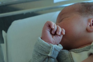 Bebek hastanedeki beşiğinde, bebeğin ellerinin detaylarına dikkat ediyor.