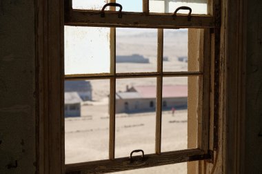 Kolmanskop hayalet kasabası, terkedilmiş bir evin penceresinden görülmüş.