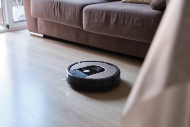 Oturma odasındaki lamine ahşap zeminde robotik süpürge, akıllı temizlik teknolojisi.