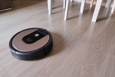 Oturma odasındaki lamine ahşap zeminde robotik süpürge, akıllı temizlik teknolojisi.