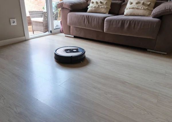 Robotic vacuum cleaner on laminate wooden floor in living room, smart cleaning technology