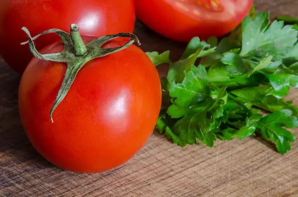 Juicy tomatoes with green-stuff on wooden table — Stock Photo, Image