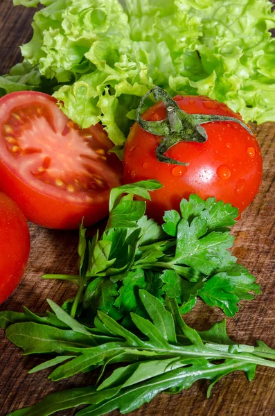 Juicy tomatoes with green-stuff on wooden table — Stock Photo, Image