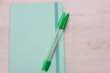 Açık yeşil defter ve iki kalem.