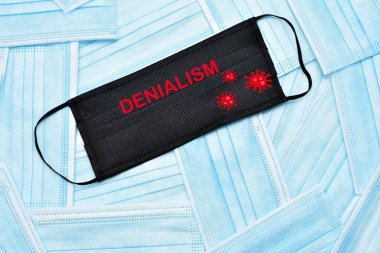 Arkaplan olarak cerrahi maskeler. Ortadaki metinde inkarcılık yazıyor. Cerrahi maske kullanımına karşı çıkan insanlar kavramı