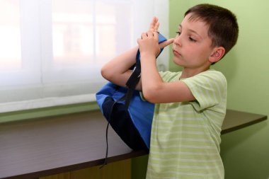 Boy putting on his backpack in his room at home