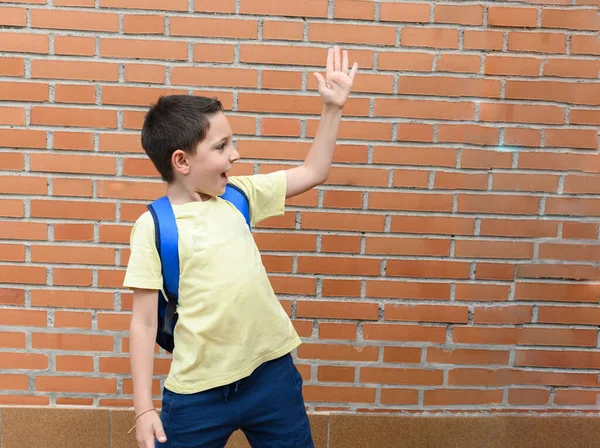 Niño Parado Con Una Bolsa Escuela Levanta Una Mano Saludo — Foto de Stock