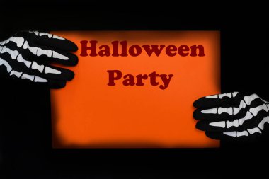 İskelet eldivenli ellerle tutulan turuncu tabela. Üzerinde Cadılar Bayramı Partisi yazan bir poster.