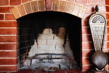 Odanın içinde doğal tuğladan yapılmış, kıvılcım ve küllükten korunan kırmızı şömine.