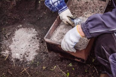 Bir erkek kül konteynırını tutar, bir kadın bitki ekmek için gübreyi toprağa doldurur.