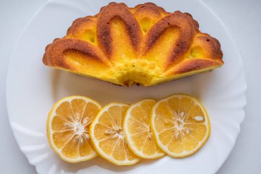 Limon dilimleriyle kaplı, beyaz bir tabakta limonlu turtanın yanında.