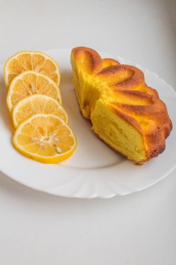 Limon dilimleriyle kaplı, beyaz bir tabakta limonlu turtanın yanında.