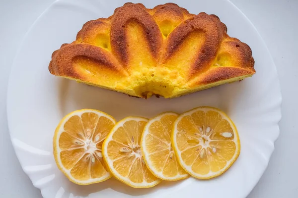 Limon dilimleriyle kaplı, beyaz bir tabakta limonlu turtanın yanında.