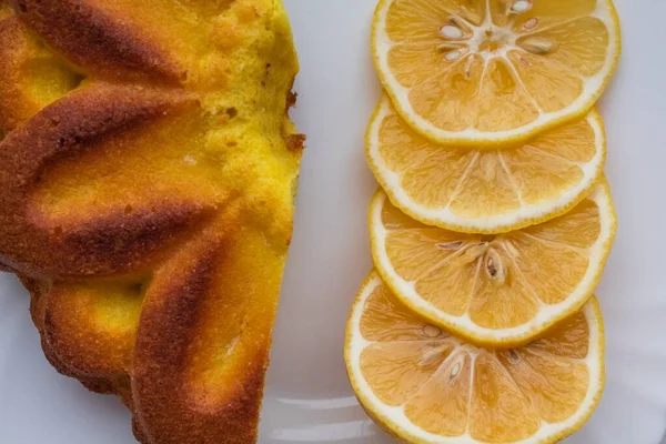 Limon dilimleriyle kaplı, beyaz bir tabakta limonlu turtanın yanında.