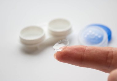 Beyaz konteynırın arka planında parmak üzerinde şeffaf lens 