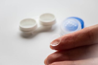 Ön planda beyaz konteynırın arka planına karşı parmak üzerinde şeffaf lens 
