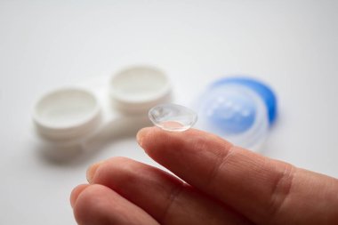 Ön planda beyaz konteynırın arka planına karşı parmak üzerinde şeffaf lens 