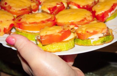 Bir kadın eli beyaz bir tabak ve fırında kabak tutar. 