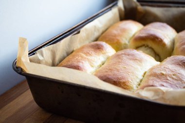 Çörekler yüksek bir fırın tepsisinde, beyaz duvarın ahşap yüzeyinde. 