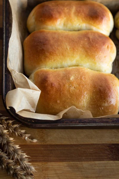 Ruddy buns in a baking tray on a wooden background — Stock Photo, Image