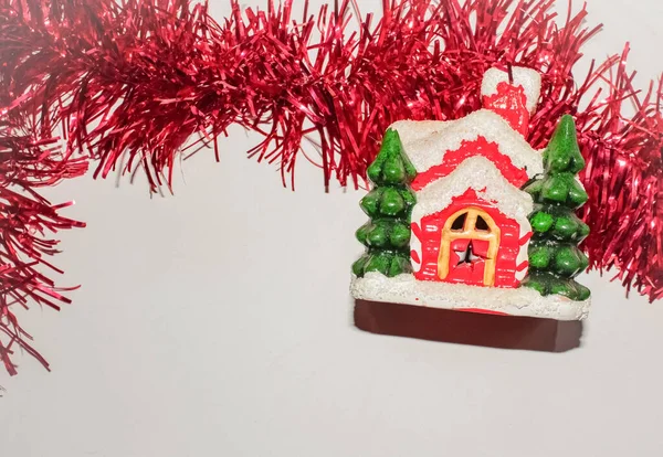 Ceramic New Years house with Christmas trees next to a fluffy red garland — Stock Photo, Image