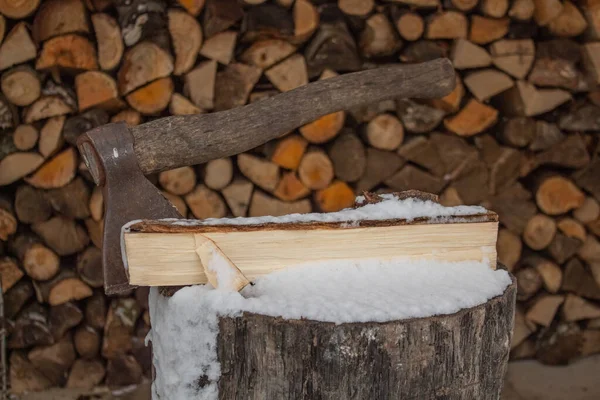 Die Axt steckt im schneebedeckten Baumstumpf vor dem Hintergrund der Struktur zur Lagerung von Brennholz — Stockfoto