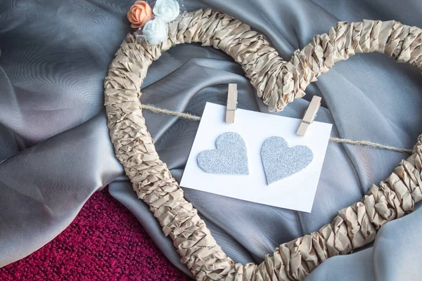 Braided frame in the shape of a heart with a card on clothespins on a gray and raspberry textile background close-up