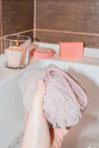Uma toalha de banho em uma mão das mulheres no banheiro contra um pano de fundo de velas e sabão — Fotografia de Stock