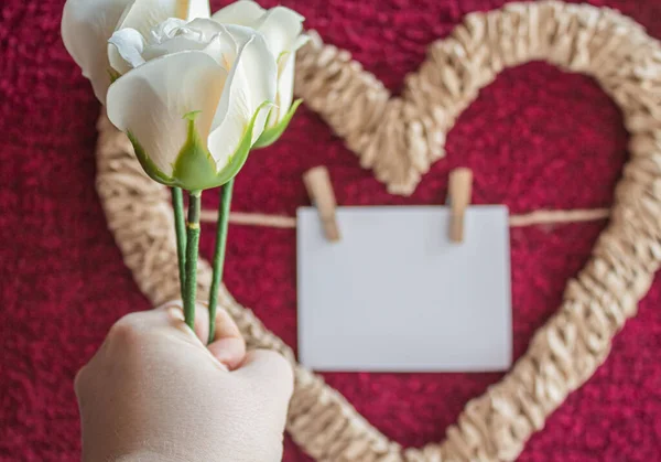 Белые розы в руке на заднем плане плетеное сердце с открыткой для фотографии или надписи — стоковое фото