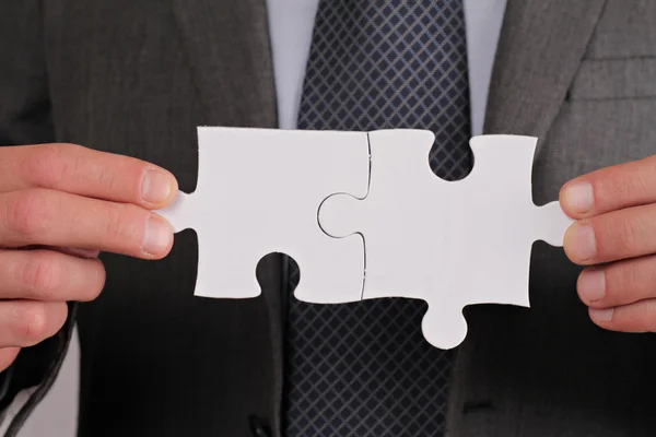 Business solutions, partnership concept. Businessman holding two pieces of a blank puzzle — Stock Photo, Image