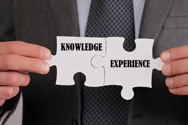 Business success concept. Connection between Knowledge and Experience, Businessman holding two pieces of a puzzle close up