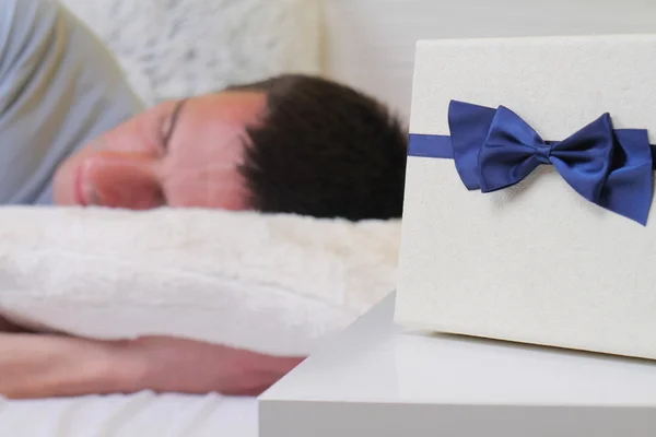 Мужчина спит с подарком на подушке рядом. Выборочный фокус. Сюрприз на день рождения — стоковое фото