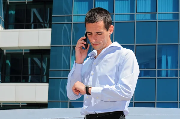 Businessman talking on the phone  in front of modern building. Businessman in a hurry looking at his watch