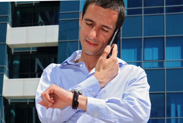 Businessman talking on the phone  in front of modern building. Businessman in a hurry looking at his watch